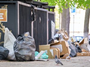 Garbage bins disposal full with litter scattered around on city street