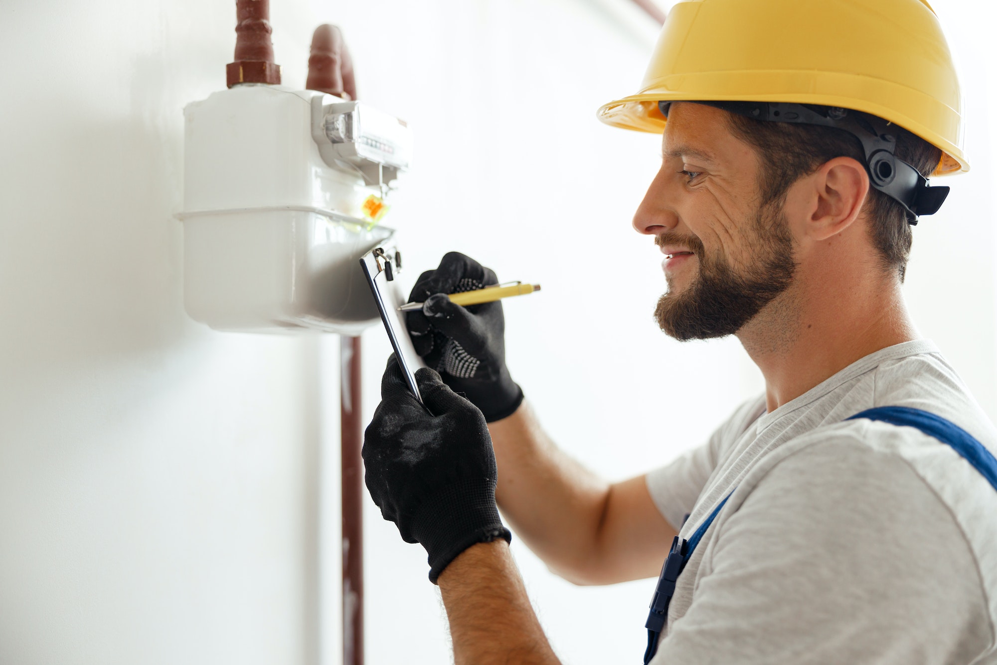 Happy professional heating fitter making notes while checking gas consumption at gas pipe and meter