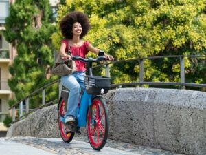 Happy black woman riding electric bicycle on city street bridge