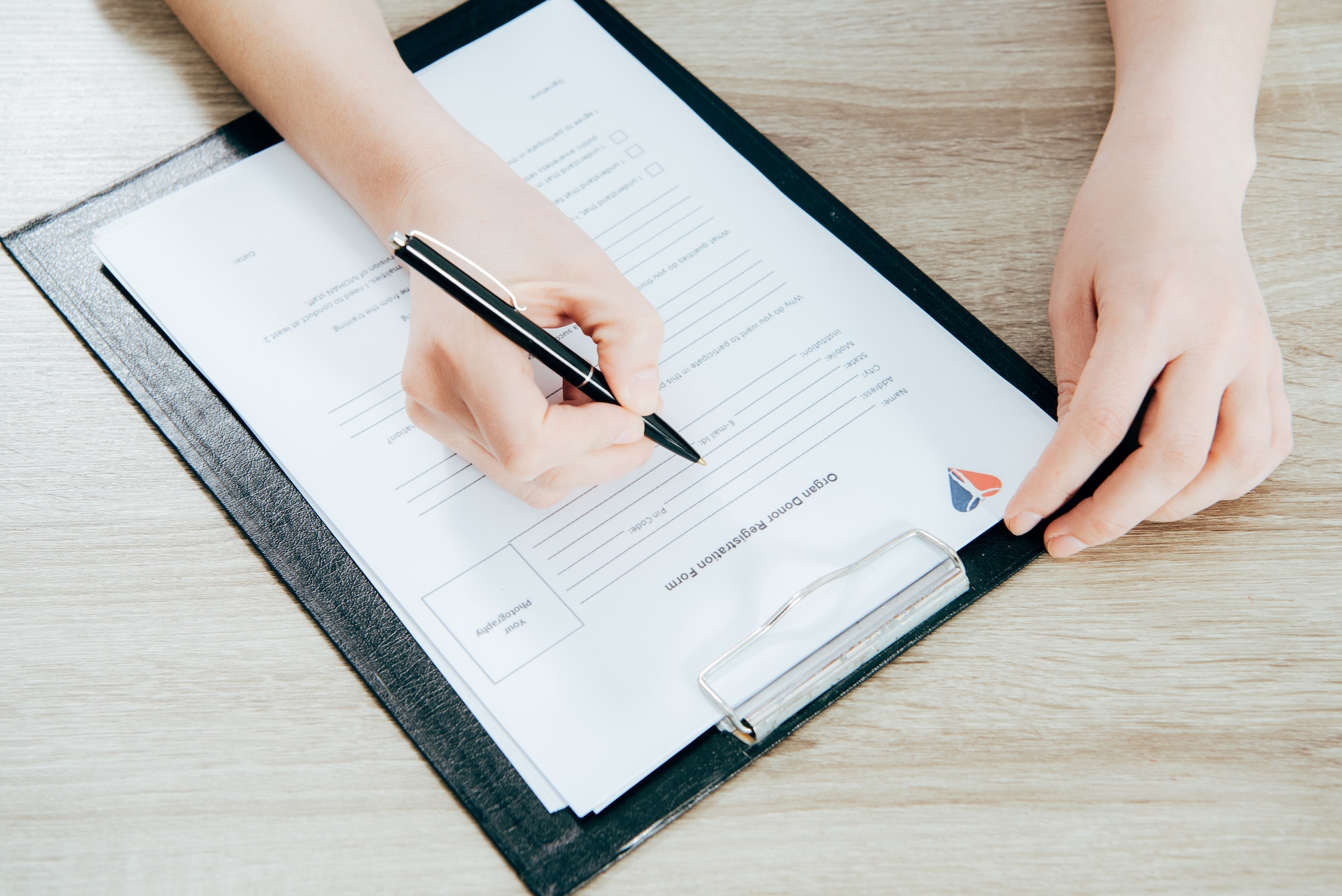 partial view of donor signing registration form on wooden surface