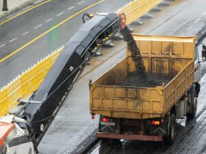 Milling machine working and removing asphalt from the road and pouring it into a truck