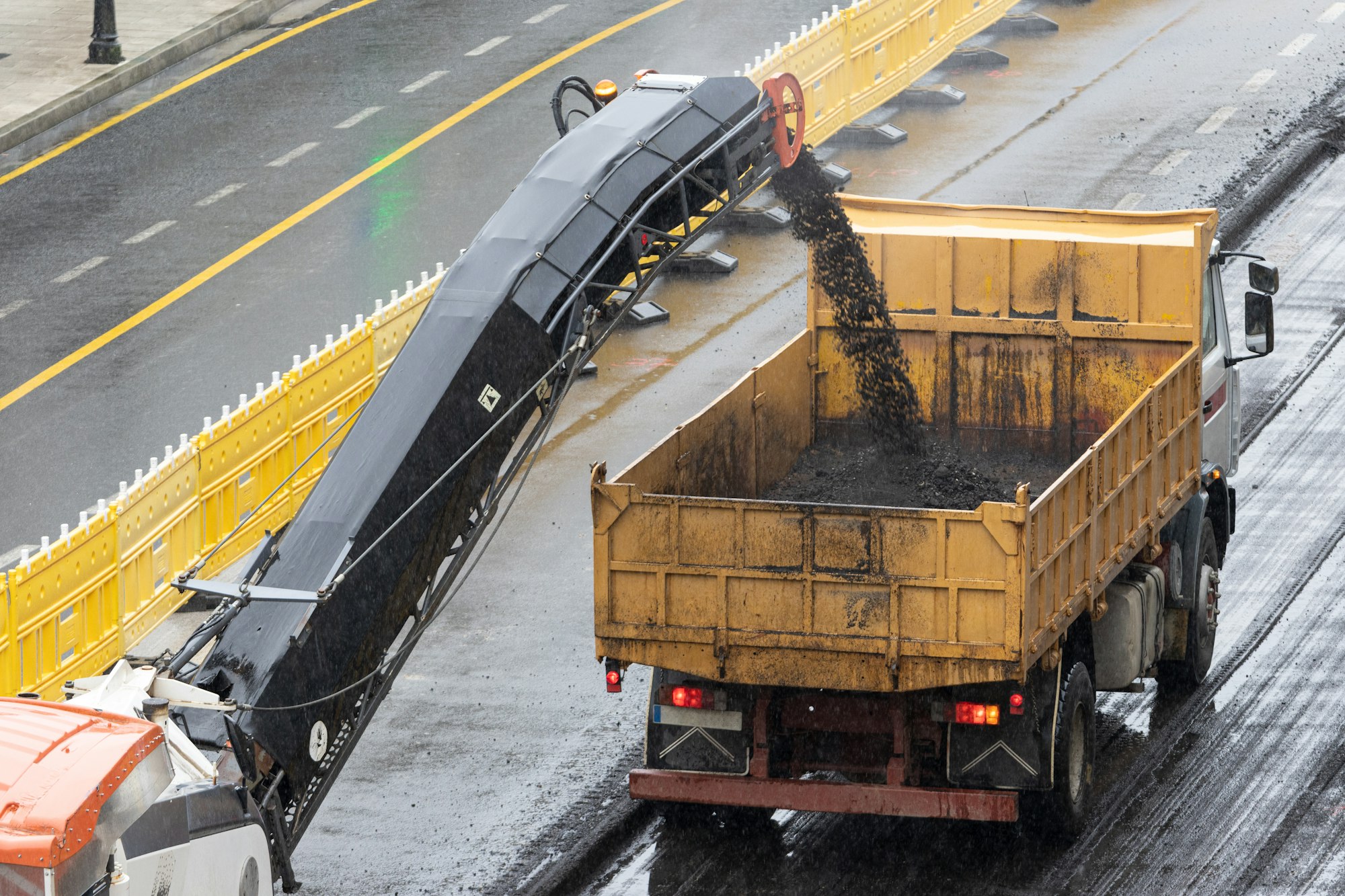 Milling machine working and removing asphalt from the road and pouring it into a truck